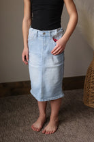 Person wearing a black top and light blue denim skirt standing on a carpeted floor.