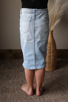 Person wearing a light blue denim skirt standing on a carpeted floor with a woven basket in the background.