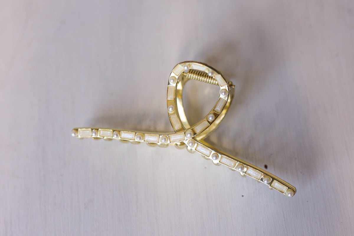 A gold-toned hair claw clip embellished with clear rectangular rhinestones, shown on a light gray background.