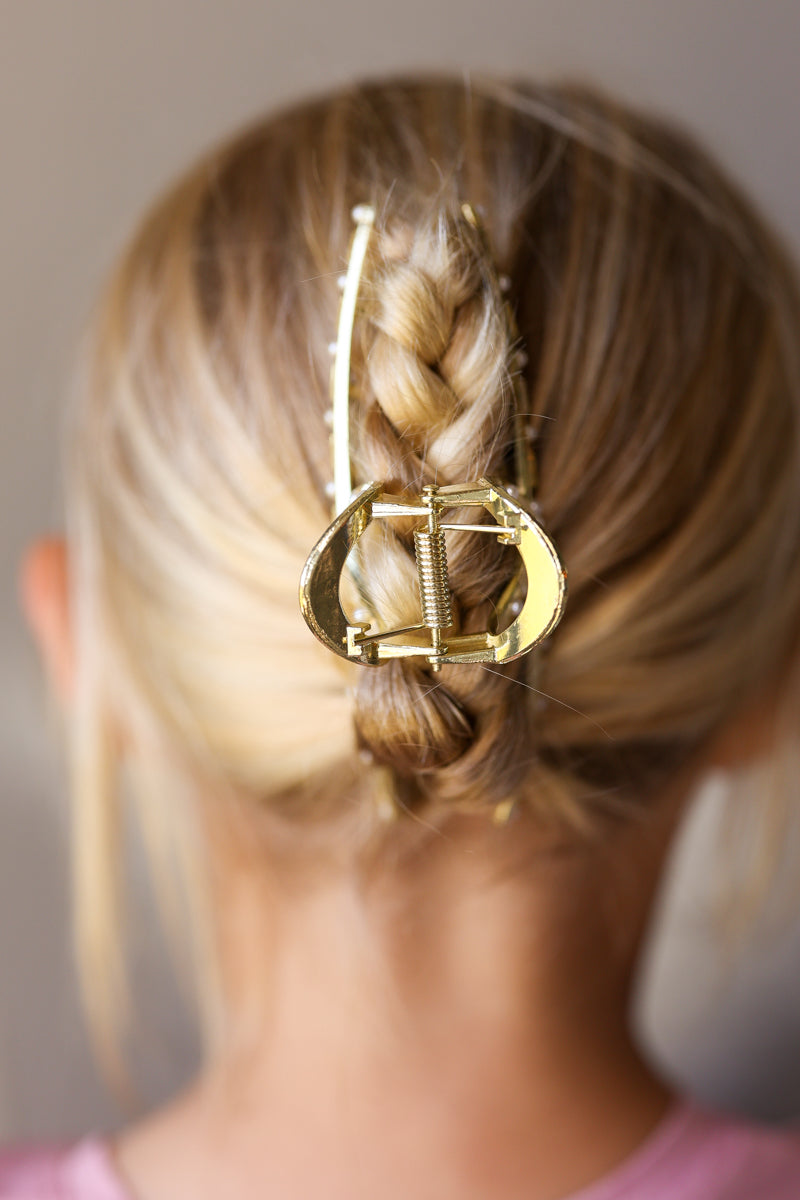 A close-up back view of a person wearing a large gold claw-style hair clip holding a braided low ponytail.