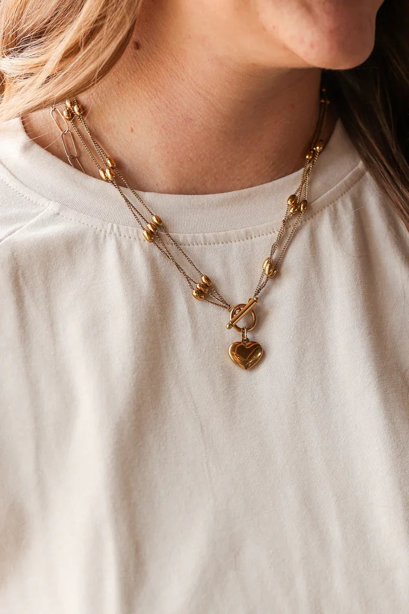 Close-up of a person wearing a gold necklace with heart pendant on a plain background