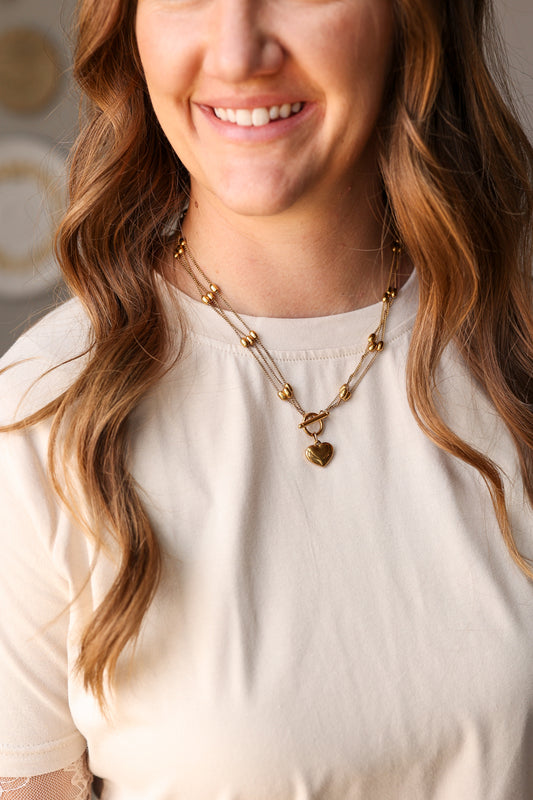 Woman wearing a gold necklace with a heart pendant, smiling.