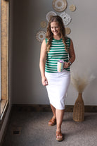 Woman wearing a green and white striped shirt and white skirt standing in a room with decorative elements.