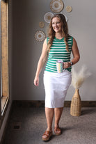 Woman in green striped shirt and white skirt holding a colorful cup in a room with decorative wall art.