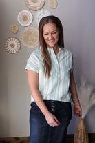 Woman wearing a light green blouse with short sleeves, standing in a room with decorative wall art.