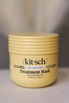 A pale yellow jar of kit-sch Treatment Mask with Coconut Oil, shown on a neutral gray background.