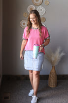 Woman in pink shirt and denim skirt holding a colorful tumbler indoors.