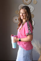 Woman holding a pink and blue tumbler with decorative wall behind her