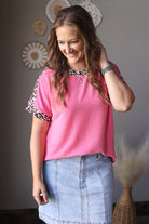 Woman wearing a pink top with leopard print sleeves in a room setting.