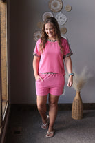 Woman in pink outfit standing in a room with decorative wall art and a vase.
