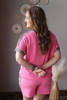 Woman wearing a pink outfit with animal print accents in a room with decorative wall art.