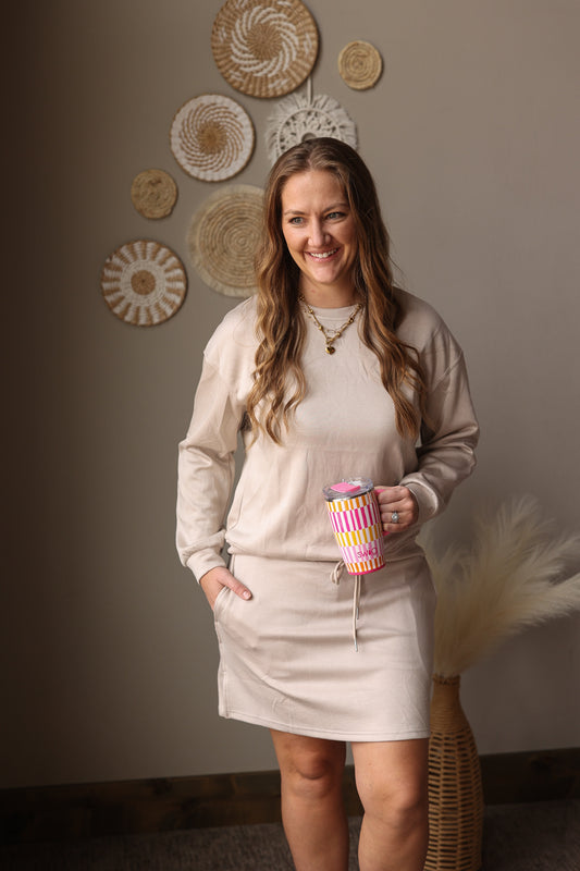 Woman holding a colorful cup in a room with decorative wall art wearing our parchment 2 piece pullover and skort set.