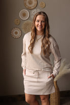 Woman wearing a beige sweater and skort standing in a room with decorative wall art.
