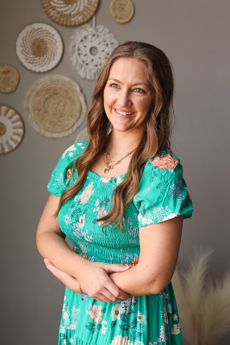 Woman in a green floral dress standing against a wall with decorative circular objects.