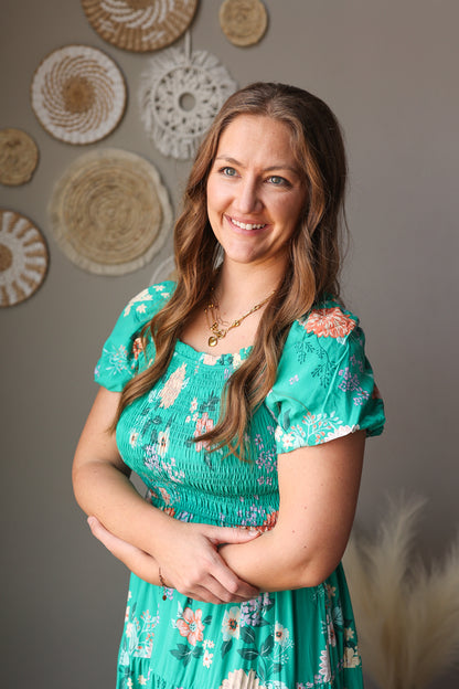 Woman in a green floral dress standing against a wall with decorative circular objects.