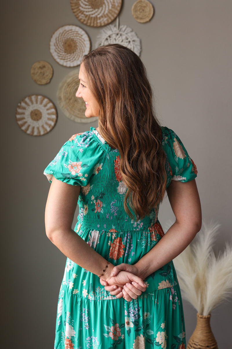Woman in a green floral dress standing against a wall with decorative circular objects.