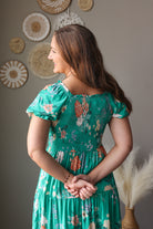 Woman in a green floral dress standing in front of decorative wall art.