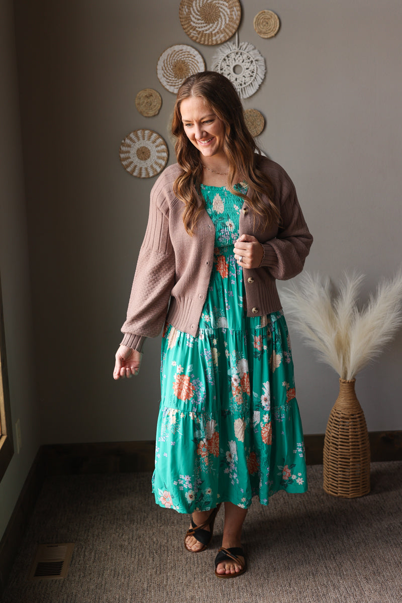 Woman in a floral dress and cardigan standing in a room with decorative wall art.