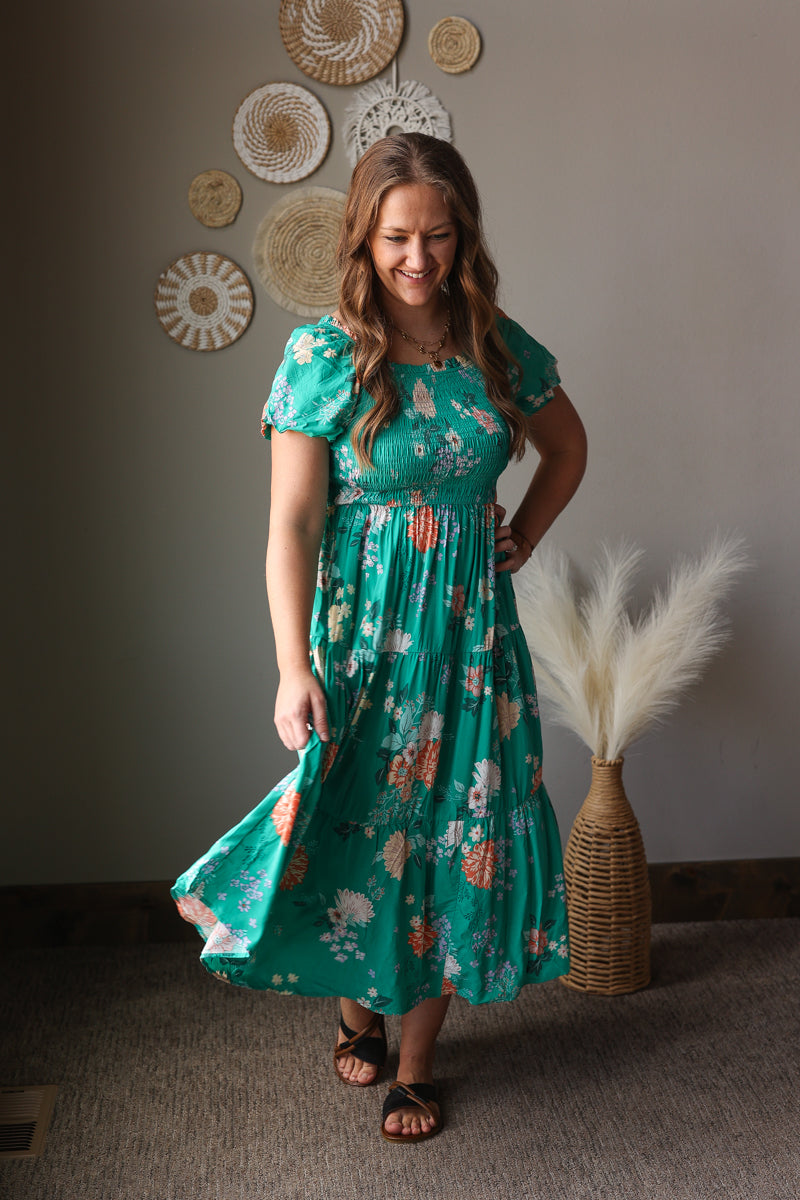 Woman wearing a teal floral dress standing in a room with decorative wall art.
