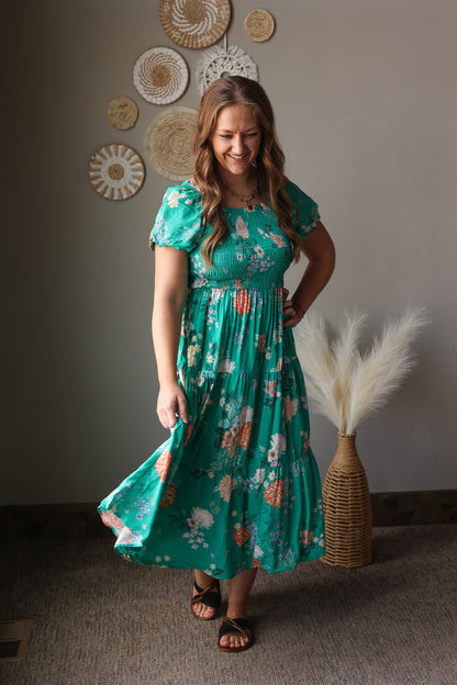 Woman wearing a teal floral dress standing in a room with decorative wall art.