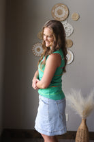 Woman in a green top and denim skirt standing in a room with decorative plates on the wall.