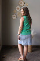 Woman wearing a green sleeveless top and denim skirt standing in a room with decorative wall art.