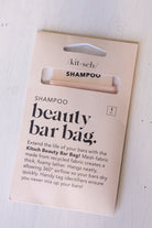 Kitsch Beauty Bar Bag Shampoo packaging card with a single beige shampoo bar visible through a cutout window, photographed on a light wood surface.