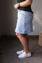 Person wearing a light blue denim skirt and white sneakers indoors.