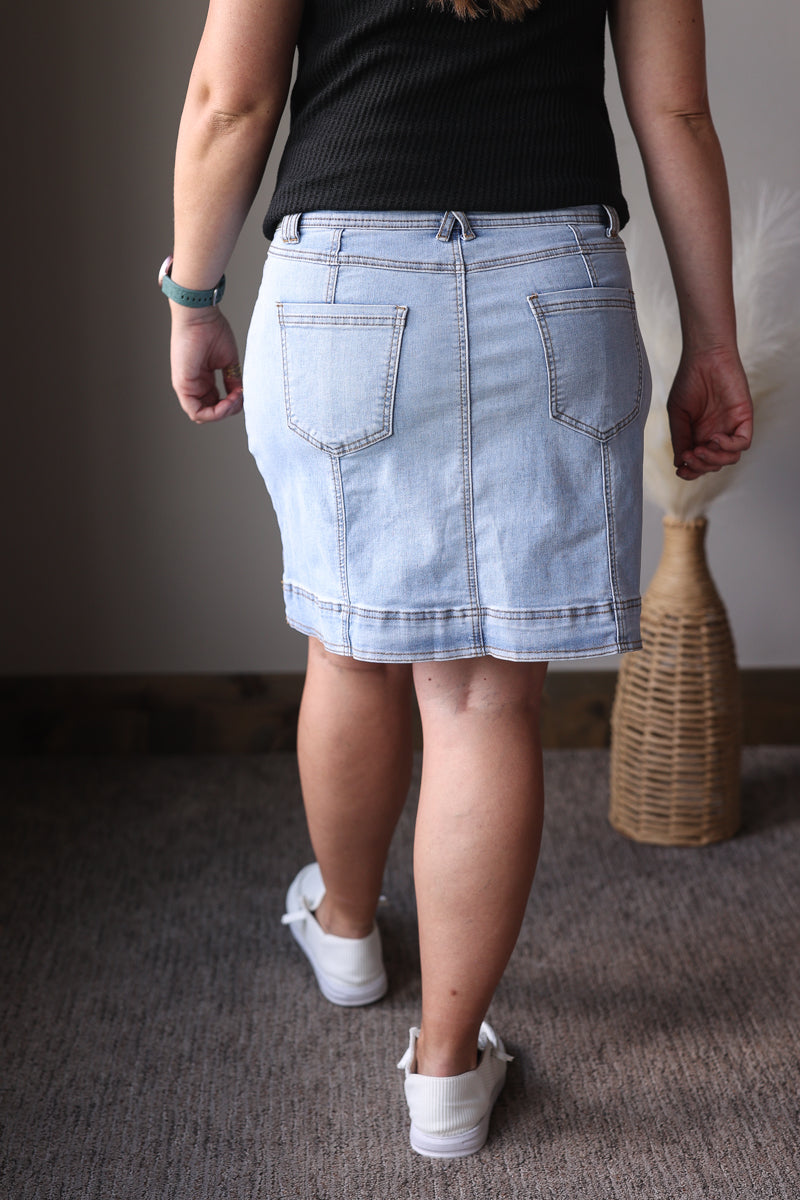 Person wearing a light blue denim skirt with a plain background