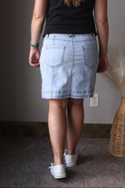 Person wearing a black top and light blue denim skirt indoors.