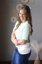 Woman wearing a green and white striped shirt with blue jean skirt standing indoors.