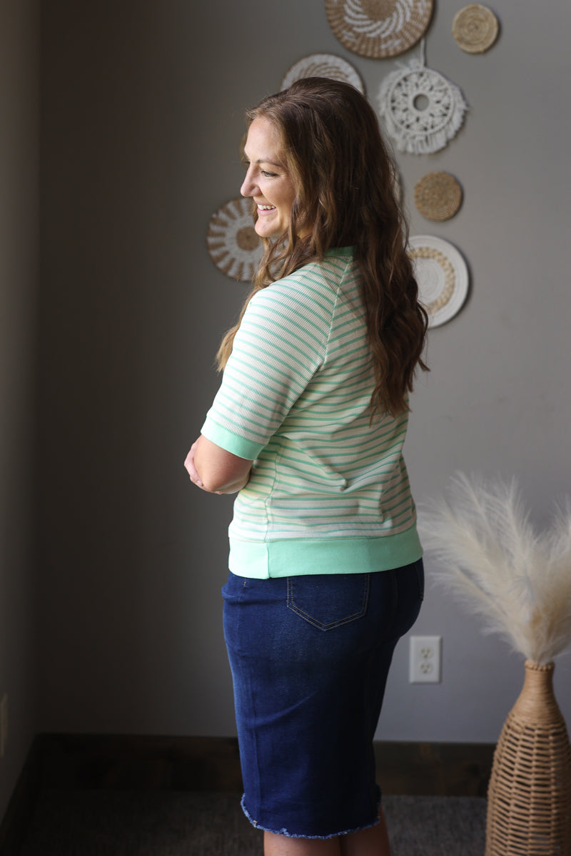 Woman wearing a striped shirt and denim skirt standing in a room with decorative plates on the wall.