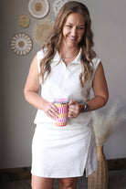 Woman in a grey 2piece skort set holding a colorful cup indoors with decorative wall art in the background.