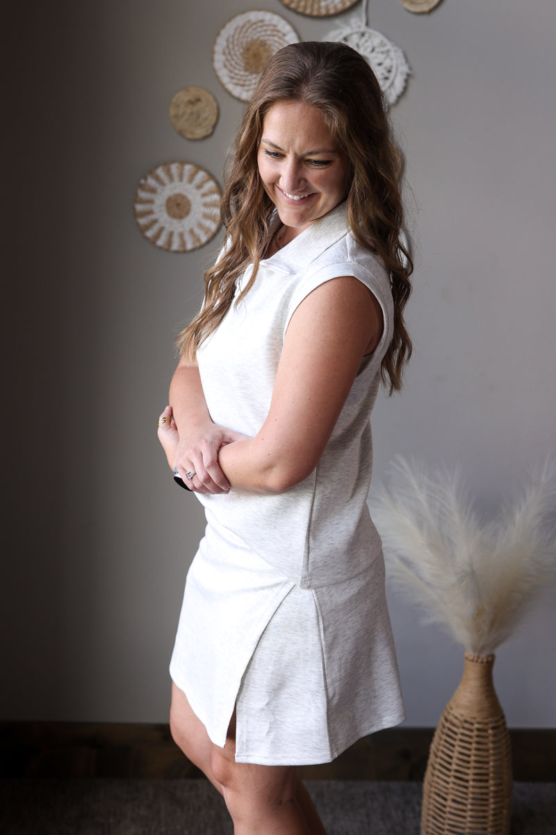 Woman in a grey sleeveless skort set standing against a neutral wall with decorative elements.
