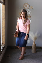 Woman in pink shirt and blue skirt standing in a room with decorative wall art.