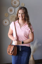 Woman in a pink shirt holding a brown leather bag in a room with decorative wall art.