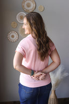 Woman wearing a pink sweater and blue jean skirt standing in a room with decorative wall art.