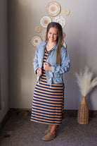 Woman wearing a denim jacket over a striped dress in a room with decorative wall art and a vase.