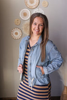 Woman wearing a striped dress and denim jacket indoors with decorative wall items.