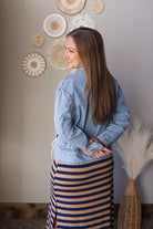 Woman wearing a denim jacket and striped skirt standing in front of decorative wall art.