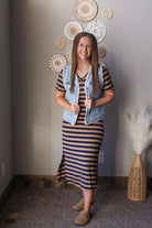 Woman in a striped dress with a denim vest standing in a room with decorative wall hangings.