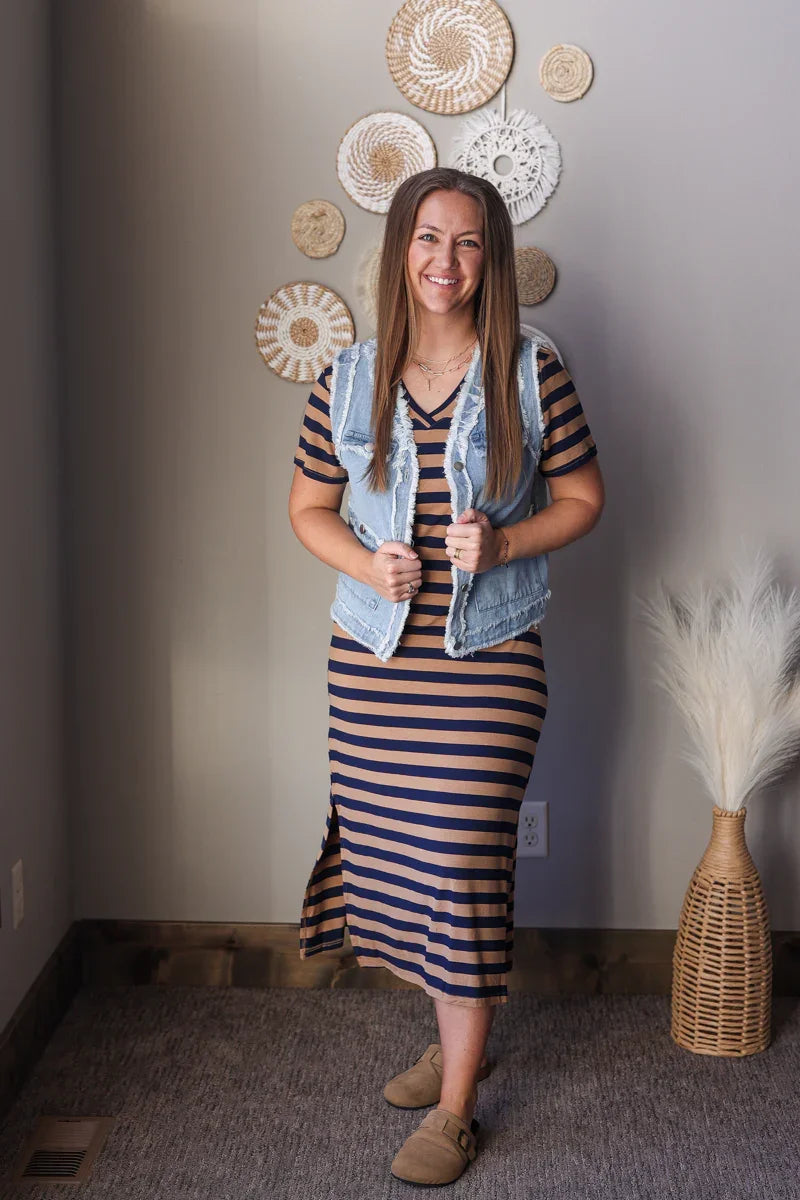 Woman in a striped dress with a denim vest standing in a room with decorative wall hangings.