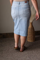 Person wearing a light blue denim skirt standing on a carpeted floor with a woven basket in the background.