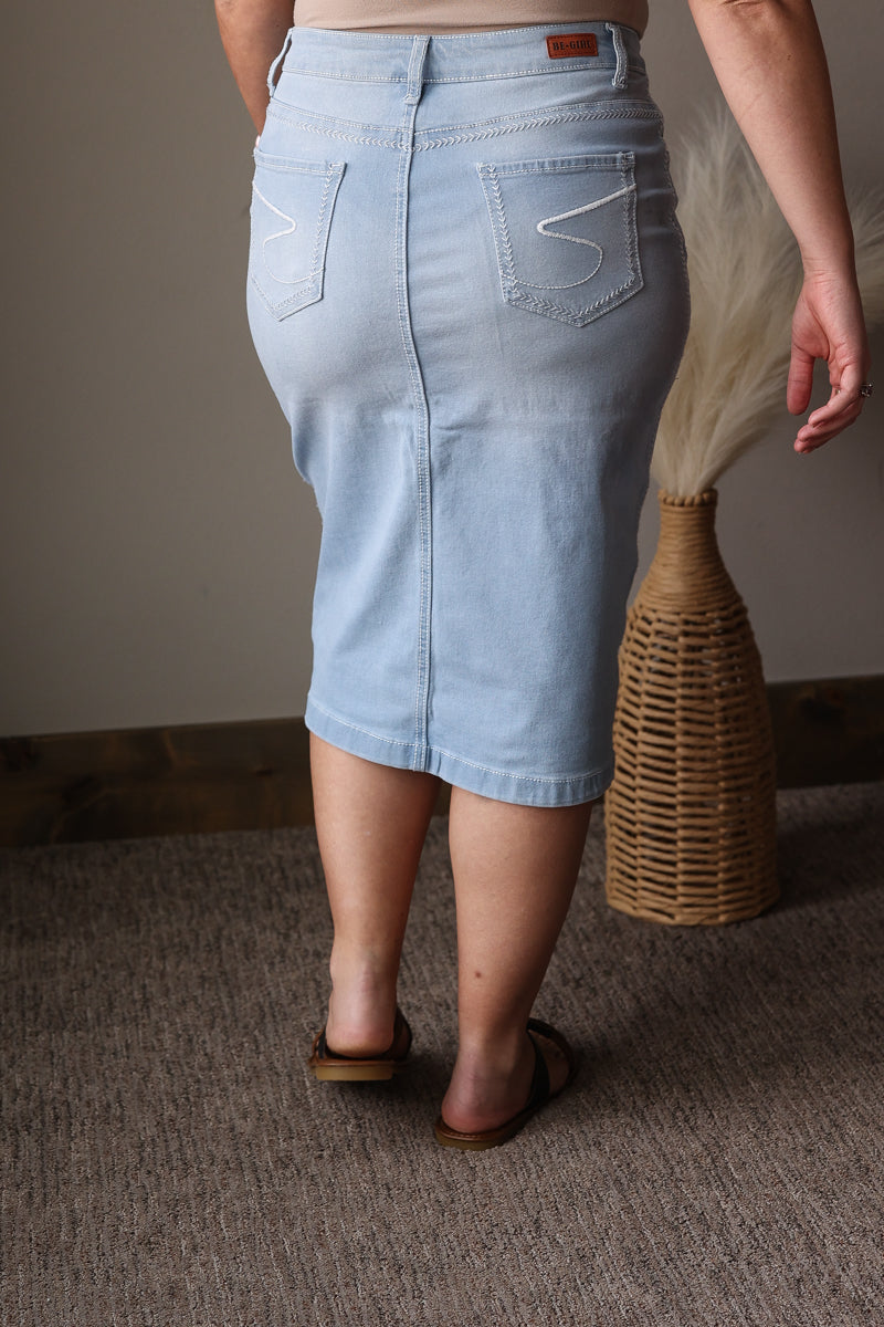 Person wearing a light blue denim skirt standing on a carpeted floor with a woven basket in the background.
