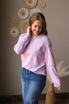 Woman wearing a pink sweater and blue jean skirt standing against a wall with decorative plates.