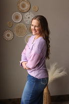 Woman in a purple sweater and blue jean skirt standing in front of decorative wall art.