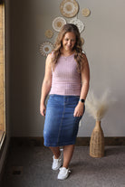Woman wearing a pink top and blue skirt standing in a room with decorative wall art.