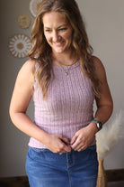 Woman wearing a pink sleeveless top and blue jean skirt, standing indoors with decorative elements in the background.