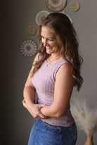 Woman wearing a pink sleeveless top and blue jean skirt standing against a neutral wall with decorative elements.
