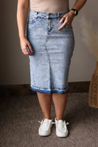 Person wearing a blue denim skirt and white sneakers indoors.